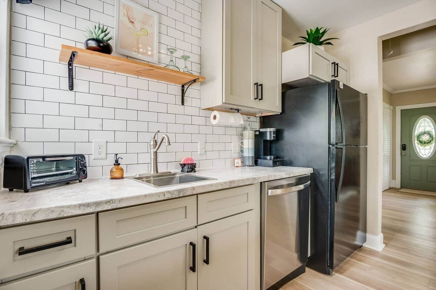 A kitchen with white subway tiles, a stainless steel refrigerator, a toaster, and a coffee maker.