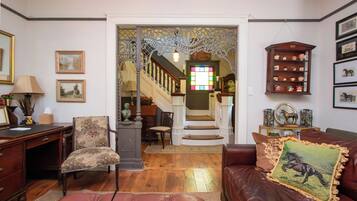 A living room with a staircase, a wooden desk, a leather sofa, and a decorative cabinet.