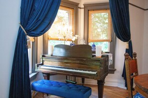 A grand piano in a room with large windows, a blue ottoman, and a wooden chair. - Fully restored historic 1911 three bedroom, two bath home in Middletown OH (Middletown)
