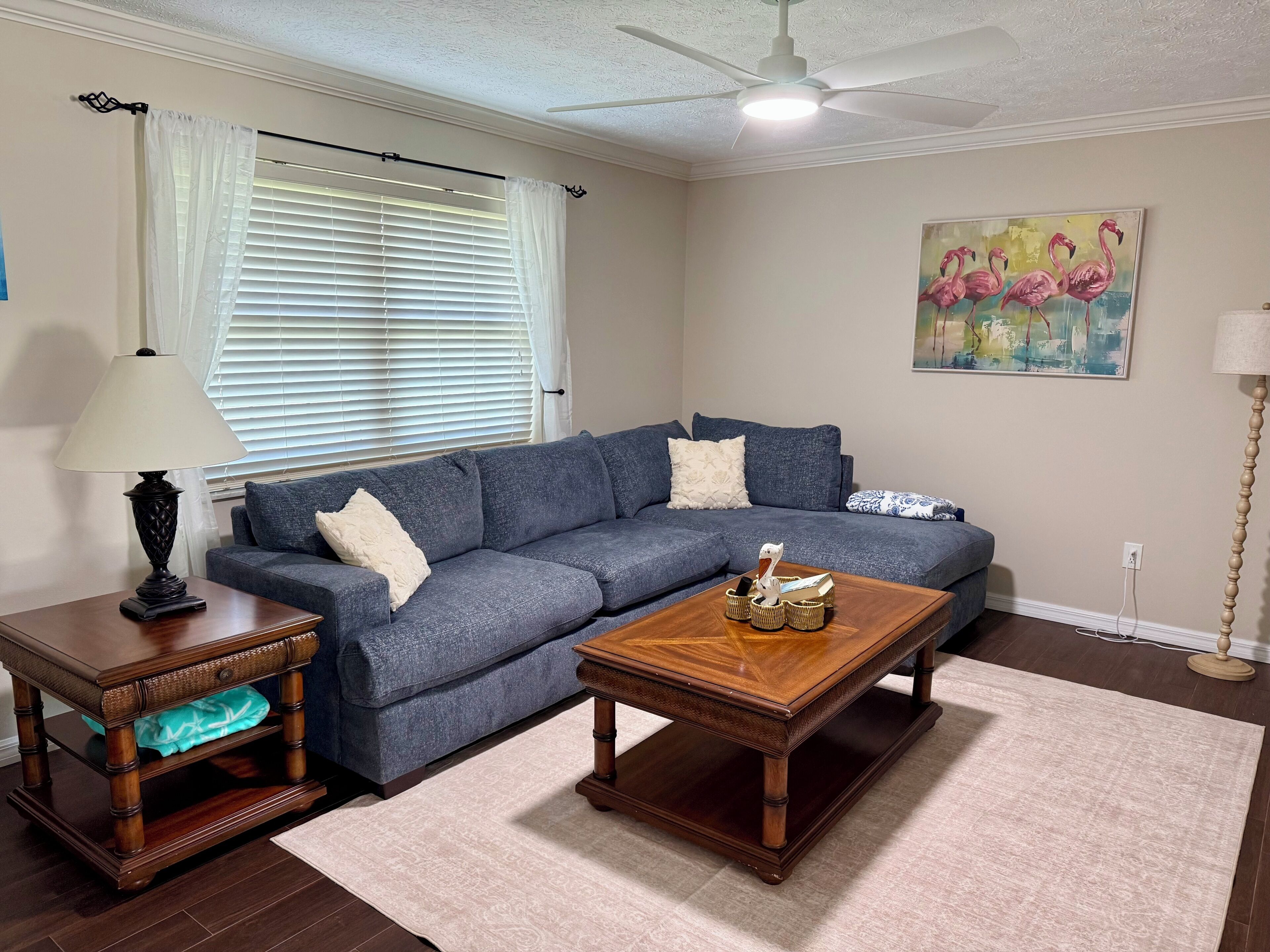 A living room with a sectional sofa, a wooden coffee table, a lamp, a painting, and a ceiling fan.