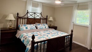 Een slaapkamer met een houten bed, twee nachtkastjes met lampen, een plafondventilator en een raam met jaloezieën.