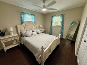 Une chambre à coucher comprenant un lit, des tables de chevet, une commode, un ventilateur de plafond et un miroir.