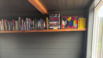 Ein graues Sofa mit einem gemusterten Teppich, ein Bücherregal mit Büchern und einer farbenfrohen, geometrischen Kiste, und ein Fenster mit Blick.