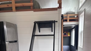 Una habitación compacta con kitchenette, una escalera, un sofá y una ventana.