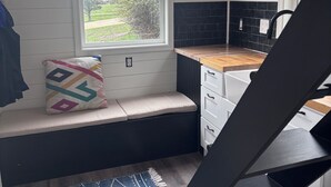 Una cocina con ventanal, un banco con cojín, una alfombra y una escalera.