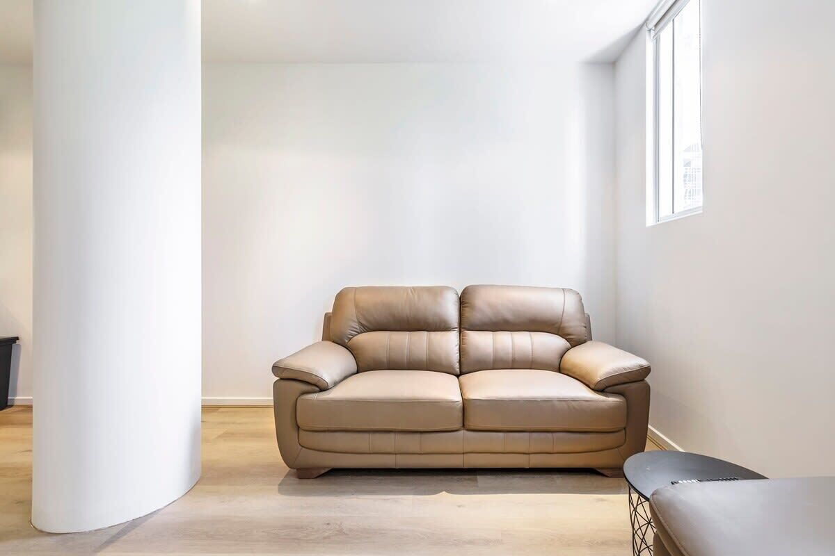 Un soggiorno moderno con un divano in pelle beige, una panca e una finestra che lascia entrare luce naturale.