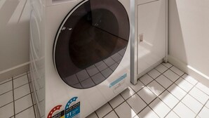 Een kleine wasruimte met een voorlader wasmachine, een klein wasbakje en een kast.