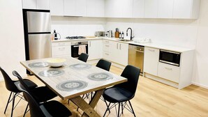 Een moderne keuken met witte kasten, een roestvrijstalen koelkast, een eettafel met zwarte stoelen en een houten vloer.