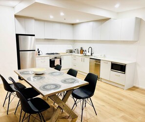 Eine moderne Küche mit weißen Schränken, einem Edelstahl-Kühlschrank, einem Esstisch mit schwarzen Stühlen und einem Holzboden.