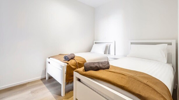 Een tweepersoonskamer met twee bedden, een houten vloer en witte wanden.