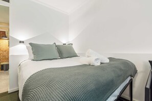 Ein ordentlich bezogenes Bett mit Kissen, einer Decke und einem gefalteten Handtuch.