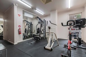 Ein Fitnessraum mit Trainingsgeräten, einem Feuerlöscher und einem Spiegel an der Wand.