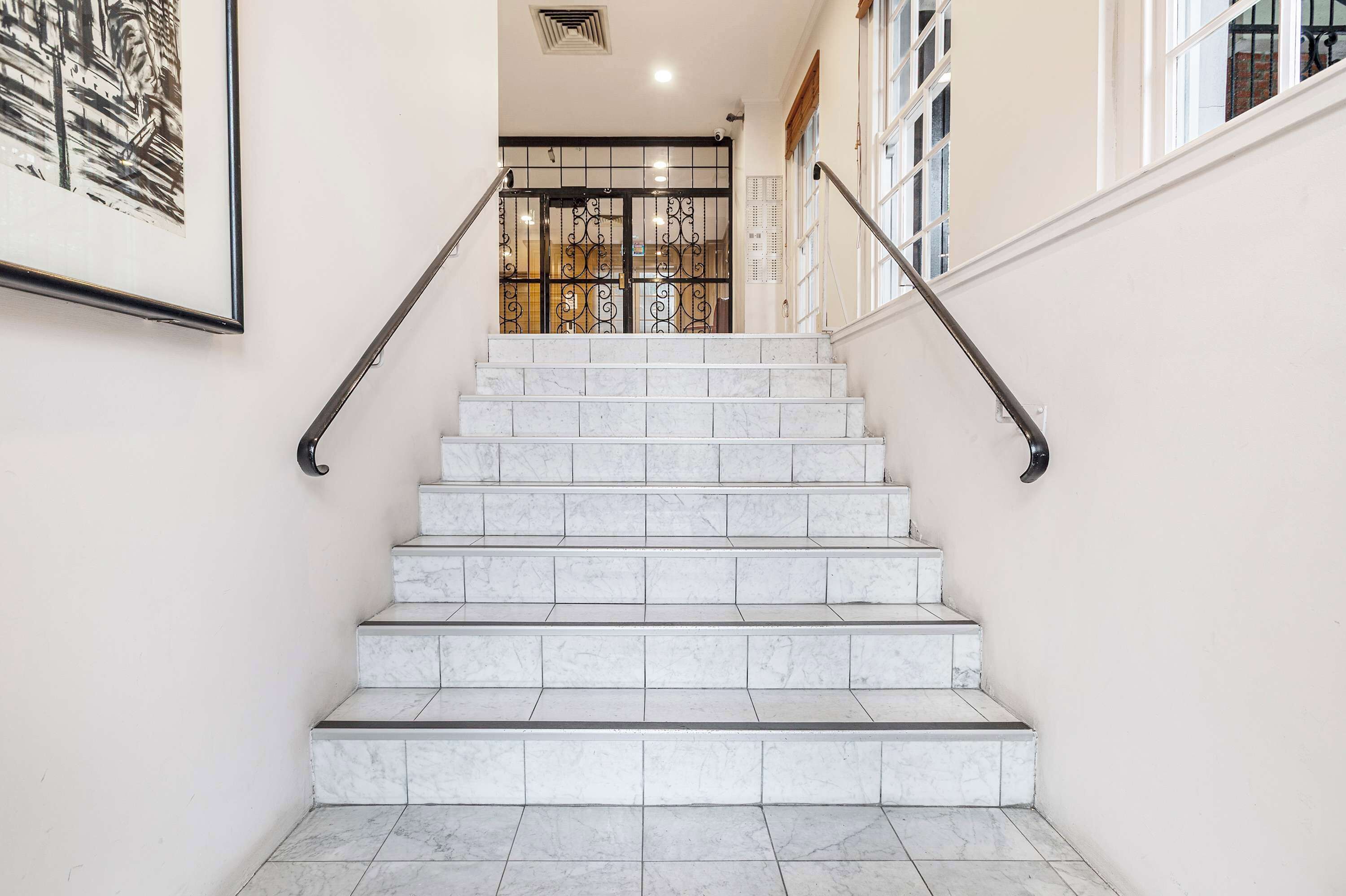 Un escalier en marbre avec des rampes en métal, menant à une porte surmontée d’un portail décoratif en métal.