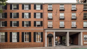 A multi-story brick building with a covered entrance, multiple windows with black shutters, and balconies with metal railings. - Stylish studio apartment opposite Carlton Gardens (Carlton)