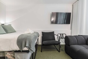 A hotel room with a bed, a chair, a sofa, and a TV mounted on the wall. - Stylish studio apartment opposite Carlton Gardens (Carlton)