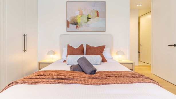 A neatly made bed with pillows and a blanket, a bedside lamp, and a painting above the bed. - Stylish, Spacious Apartment in Malvern (Malvern)