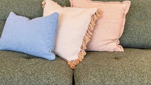 A green sofa with two pillows, one blue and one pink, and a colorful abstract painting on the wall. - Stylish, Spacious Apartment in Malvern (Malvern)