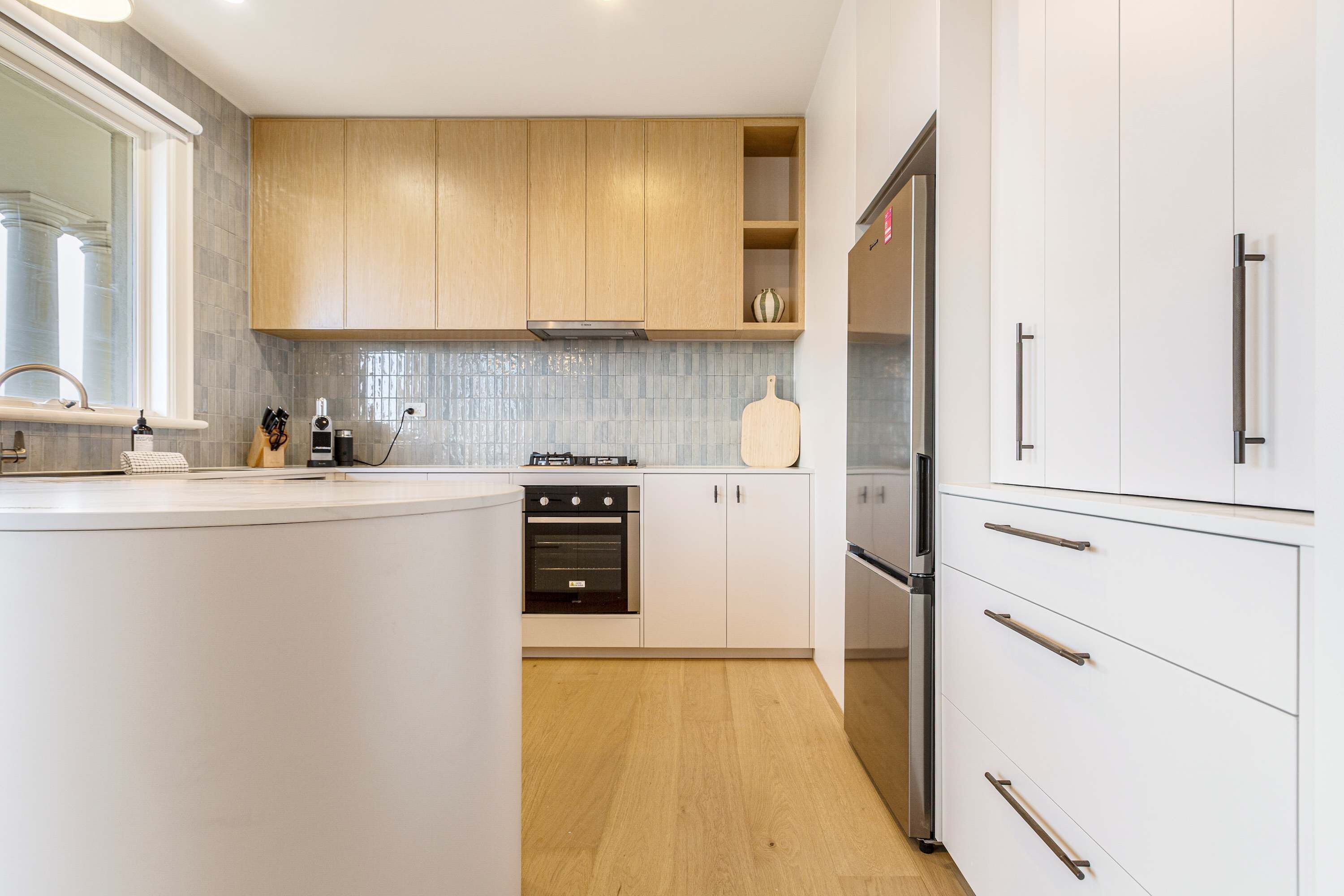 A modern kitchen with white cabinets, a stainless steel refrigerator, and a wooden countertop.