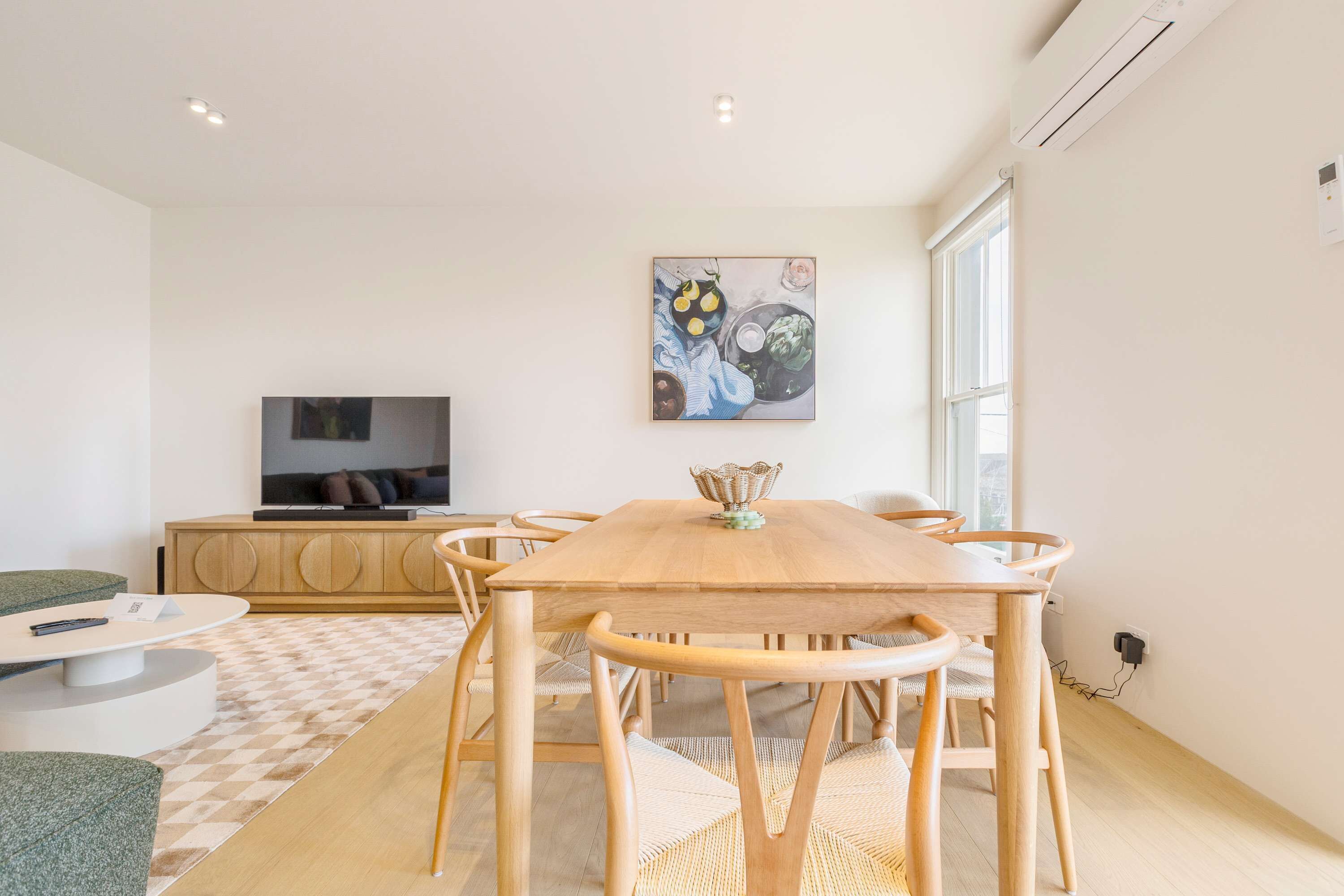 A modern living room with a wooden dining table, chairs, a sofa, and a TV.