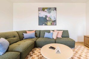 A sectional sofa with multiple cushions, a round coffee table, and a painting on the wall. - Stylish, Spacious Apartment in Malvern (Malvern)