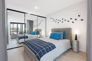 A modern bedroom with a large bed, bedside tables, a mirror, and a wall with bird decals. - Stylish 1 Bedroom Apartment (North Melbourne)