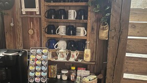 A rustic kitchen with a coffee machine, mugs, and a variety of kitchen items on shelves.