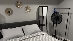 Ein Schlafzimmer mit einem Bett, einem Standventilator und Wanddekoration.