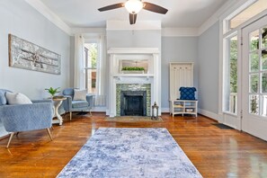 A living room with a fireplace, a ceiling fan, and a large window. - Adorable 4-3 close to EVERYTHING! (Birmingham)
