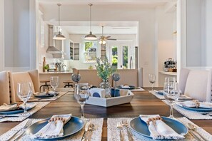 A dining room with a wooden table set for four, surrounded by chairs, with a view of the kitchen and a dining area in the background. - Adorable 4-3 close to EVERYTHING! (Birmingham)