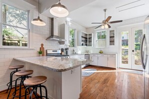A modern kitchen with a central island, bar stools, and a ceiling fan.