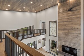 A multi-level interior with wooden flooring, a staircase with a wooden railing, and a flat-screen TV mounted on a wooden wall. - Spacious 4-bedroom house in tranquil Lead with AC and game room (Lead)
