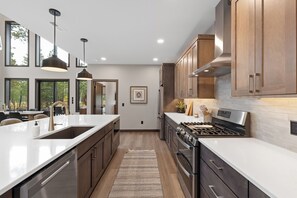 A modern kitchen with stainless steel appliances, wooden cabinets, and a large island with a sink. - Spacious 4-bedroom house in tranquil Lead with AC and game room (Lead)