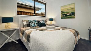 Ein Schlafzimmer mit einem Bett, zwei Nachttischen, einem Fenster und einem Bild an der Wand.