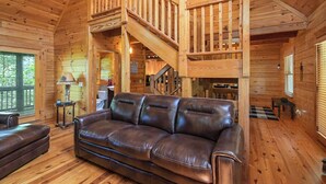 A wooden cabin interior with a leather sofa, wooden staircase, and a view of the outdoors. - Peaceful 3-bedroom mountain cabin in the charming & gated Talking Rock Resort. (Talking Rock)