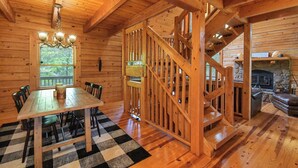 A wooden interior with a dining table, chairs, a chandelier, a staircase, and a fireplace. - Peaceful 3-bedroom mountain cabin in the charming & gated Talking Rock Resort. (Talking Rock)