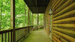 A wooden cabin with a covered porch, a railing, and a view of the surrounding forest. - Peaceful 3-bedroom mountain cabin in the charming & gated Talking Rock Resort. (Talking Rock)
