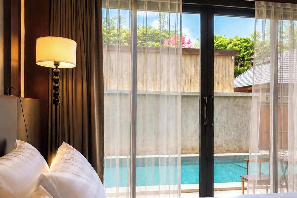Habitación de hotel con una cama grande, un escritorio, una lámpara y vistas a una piscina.
