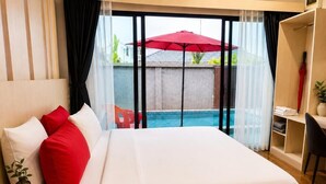 Habitación de hotel con cama, escritorio, silla, un paraguas rojo y vista a una piscina.