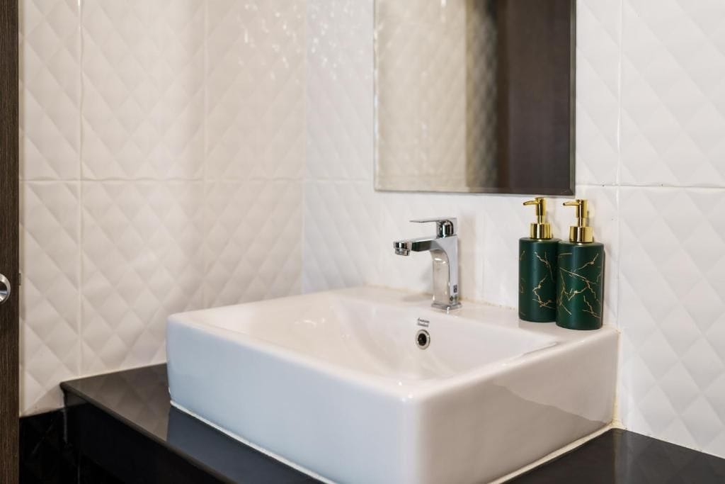 Un baño con lavabo blanco, espejo y dos dispensadores de jabón de mármol verde.