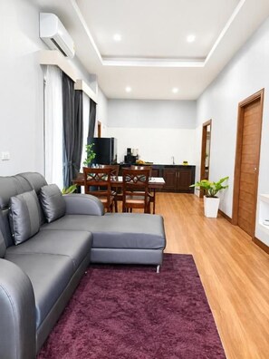 Una sala de estar moderna con un sofá seccional gris, una mesa de comedor con sillas, una zona de cocina y piso de madera.