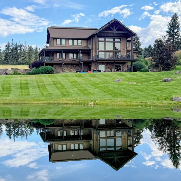 A large, two-story house with a balcony, a lawn, and a pond in front.