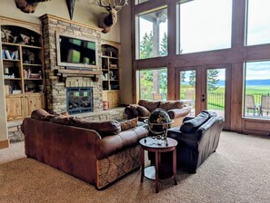A living room with a stone fireplace, leather sofas, a globe on a small table, and a large window overlooking a landscape.