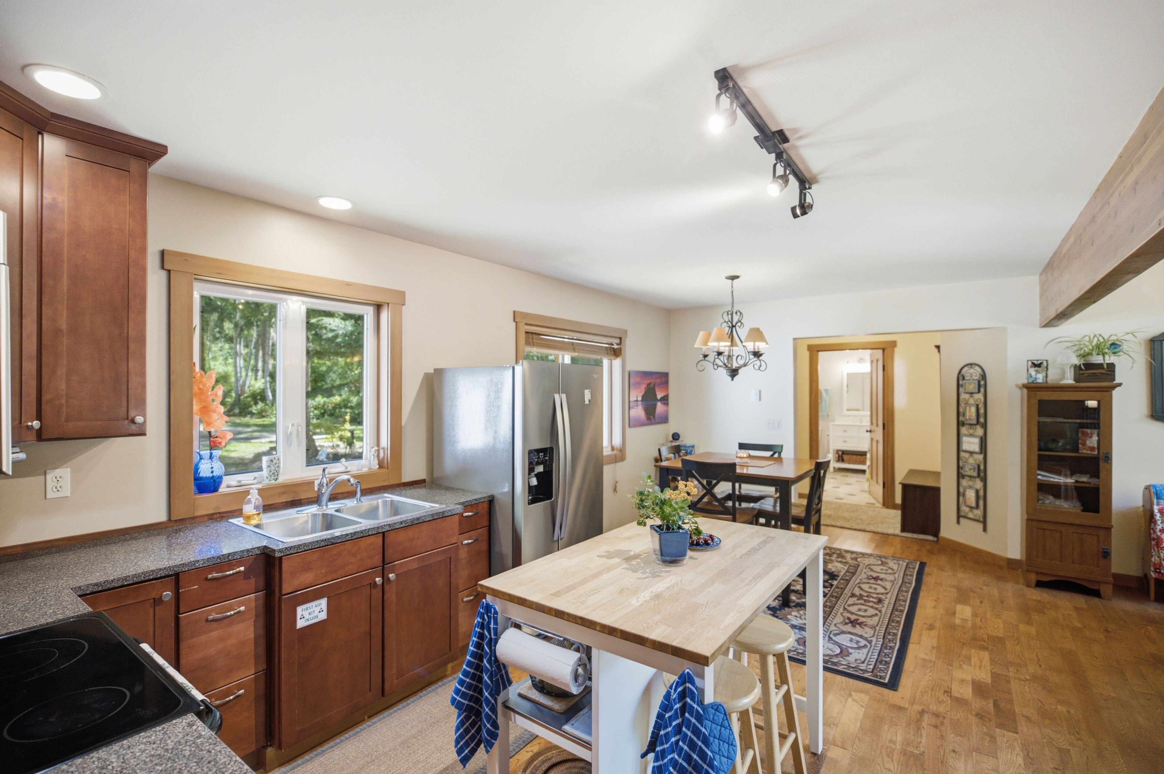 A kitchen with wooden cabinets, a stainless steel refrigerator, a sink, and a dining area with a table and chairs.