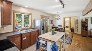 Une cuisine dotée de meubles en bois, d’un réfrigérateur en acier inoxydable, d’un évier et d’un coin repas avec une table et des chaises.