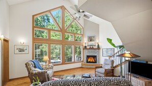 Un salon spacieux doté d’une cheminée, de grandes fenêtres et d’un ventilateur de plafond.