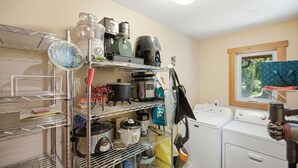 Un espace buanderie comprenant un lave-linge, des sèche-linge et une étagère métallique où sont rangés des appareils de cuisine.