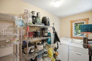 A laundry area with a washing machine, dryers, and a metal shelving unit with kitchen appliances. - Beachcombers Island Hideaway (Marrowstone)