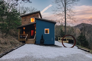 A cabin with a wooden exterior and a blue section, surrounded by trees and a gravel path. - Luxury Cabin + Salt Wall, Sauna & Hot Tub (Stanton)