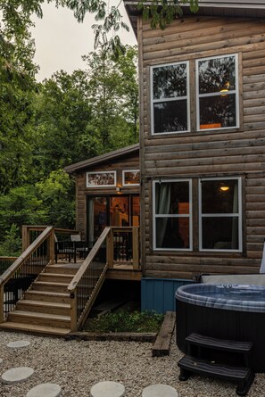 Eine zweistöckige Holzhütte mit einer Terrasse und einem Whirlpool.