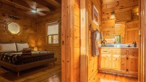 Ein Holzblockhaus-Innenraum mit Bett, kleinem Fenster und Küchenzeile.